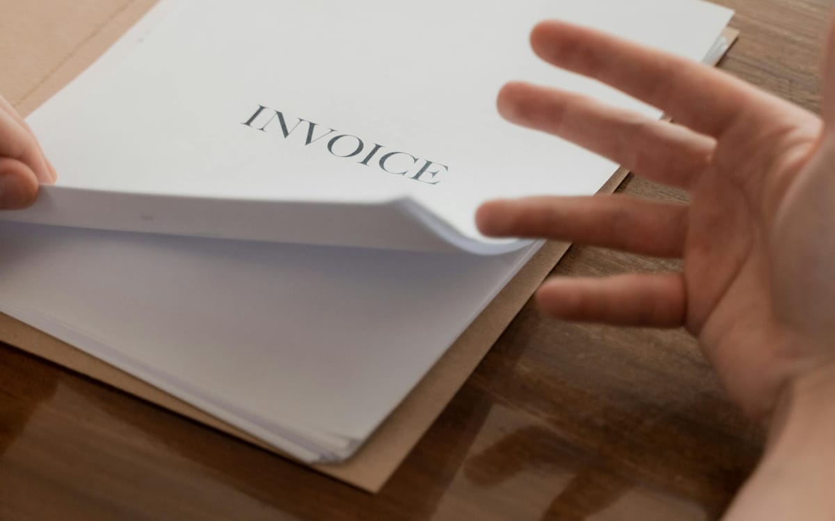 A founder's hand turning through a stack of paper invoices on a wooden desk — the source documents behind the books that an audit and Profits Tax Return are built on