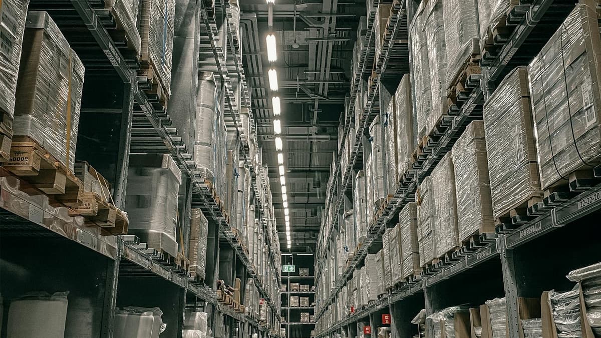 A tidy fulfillment warehouse aisle lined with tall shelving full of boxed inventory and pallets — the stock behind a multi-marketplace Amazon FBA operation