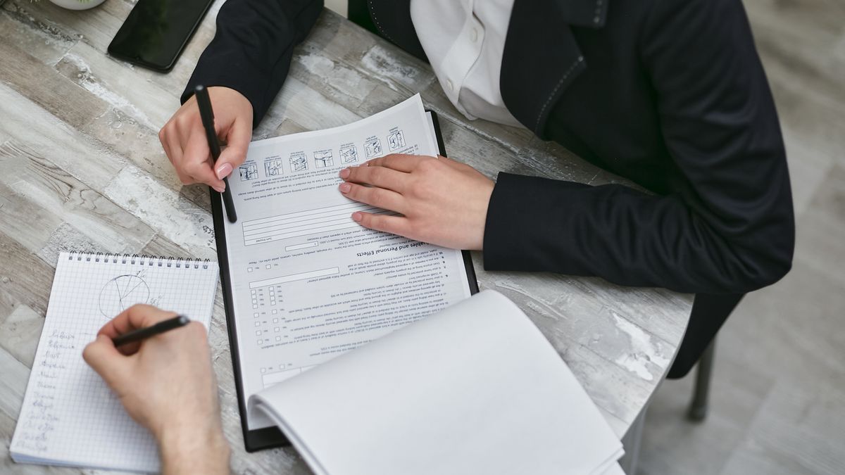 Two people reviewing a business document together at a desk, one annotating a checklist — rebuilding a bank application file after a rejection
