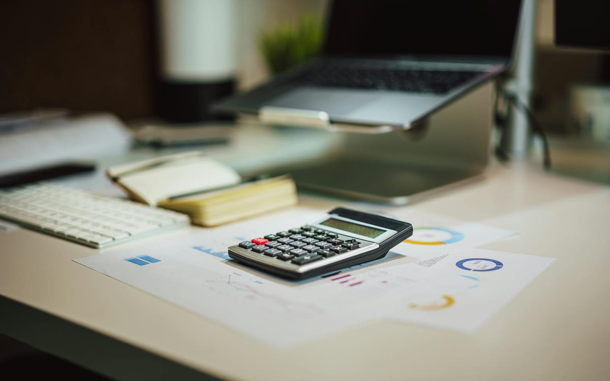 A calculator resting on printed financial charts beside a laptop on a tidy desk — the kind of money-flow evidence that strengthens a Hong Kong bank account application