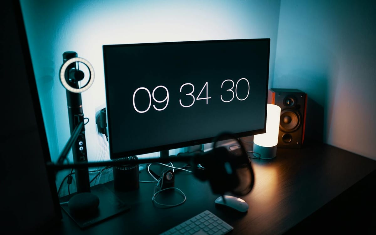 A creator's desk at night — a monitor, a small ring light and studio speakers lit by soft ambient light, the kind of remote setup a course business runs on