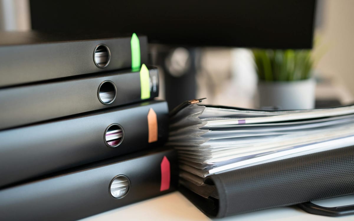 Labelled ring binders with colour-coded tabs and a file of documents on an office desk — the organised bookkeeping and statutory records that evidence a company's substance