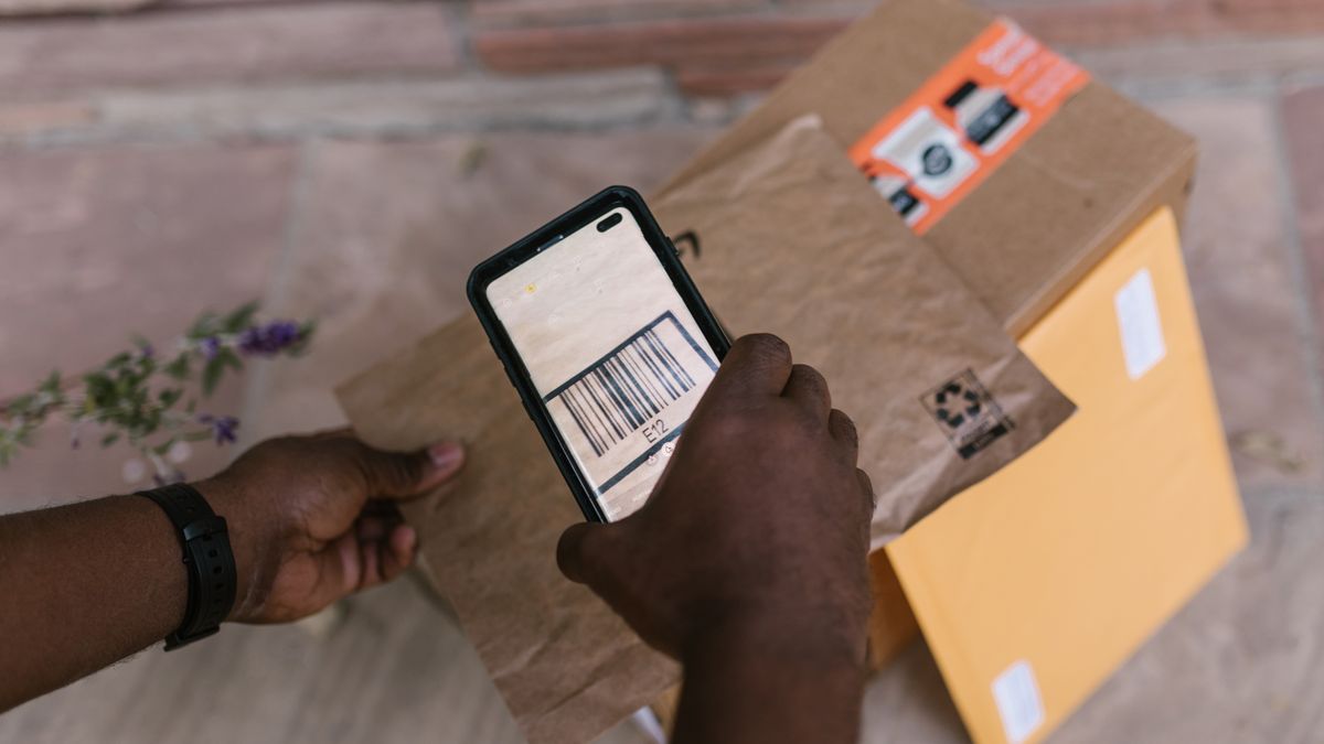 A seller scanning a parcel's barcode with a smartphone beside packed orders — the shipping side of a cross-border online store