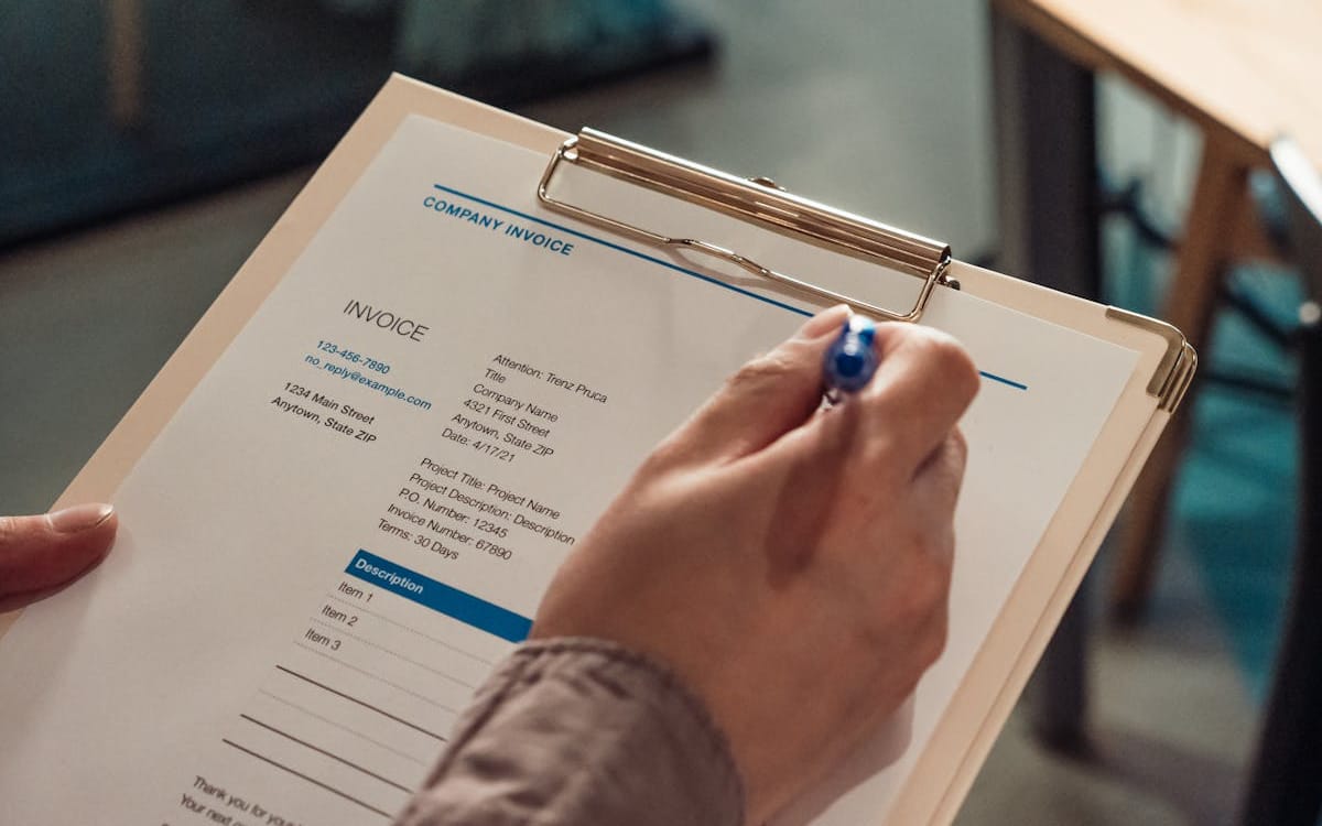 A company invoice on a clipboard being completed with a pen — the credible, business-named billing document a Hong Kong limited company lets a one-person agency issue