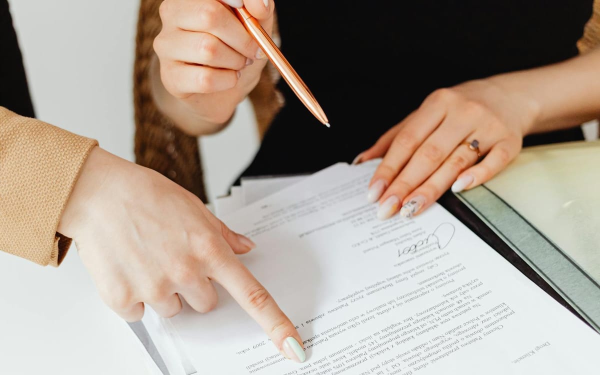 Two people reviewing and signing a business contract together at a desk with a binder and coffee — a founder formalising the next stage of a growing business